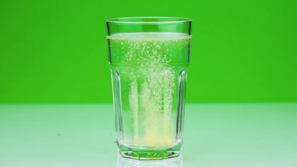 An effervescent tablet against pain falls into a glass and dissolves Close-up slow-motion shot of aspirin on a green background - Footage, Video