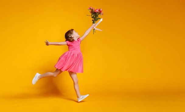 funny child girl runs and jumps with bouquet of flowers on color - Photo, Image