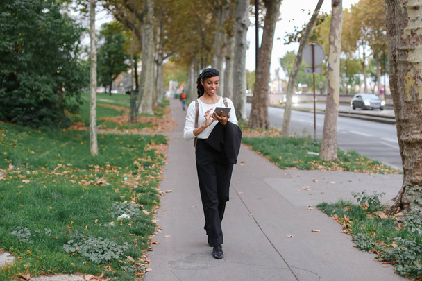 Studente felice afro-americano che cammina con tablet nel parco autunnale, indossando lo zaino
. - Foto, immagini