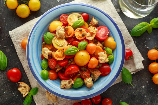 Homemade Panzanella, Tomato traditional Italian salad with red, yellow, orange cherry tomatoes, capers, basil and ciabatta croutons. summer healthy food. - Photo, Image