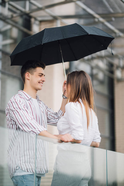 Una joven pareja de amantes bajo un paraguas en la ciudad. Gente guapa divirtiéndose en el centro urbano de la ciudad en un día de lluvia. Amor y concepto de vacaciones
 - Foto, Imagen