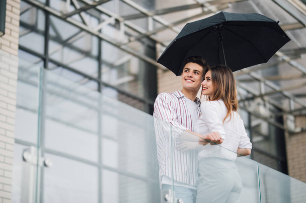 Молодая красивая пара смотрит друг на друга с любовью под зонтиком в дождливый день на улице. Понятие любви и отношений в паре
. - Фото, изображение