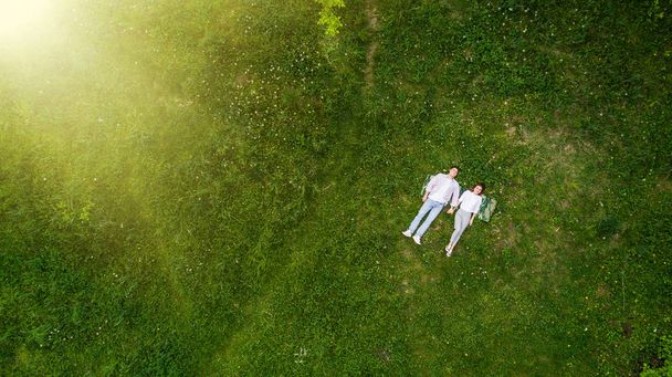 Romantisch in liefde paar jonge mensen liggen op gras in park houden handen samen weergave van bovenaf. - Foto, afbeelding