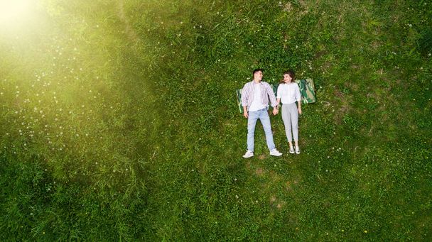 Beautiful in love young couple lying on the grass, view from above - Фото, изображение