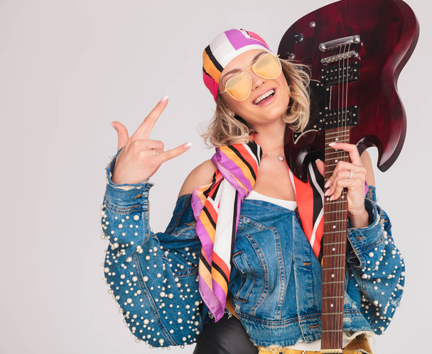 mulher faz rock no sinal enquanto segura guitarra no ombro
 - Foto, Imagem