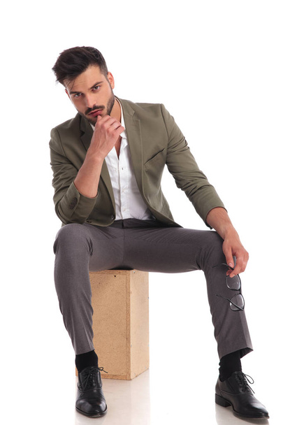 seated man with green suit posing seductively while holdin chin - Φωτογραφία, εικόνα