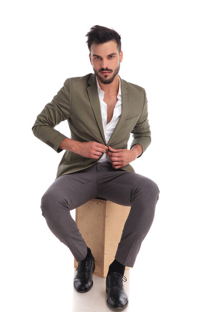 handsome elegant man unbuttoning suit jacket while sitting - Фото, зображення