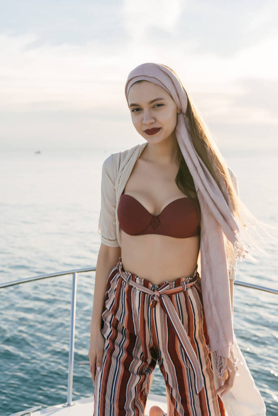 confident beautiful girl with a headscarf on her head posing on a white yacht, enjoying a rich life - 写真・画像