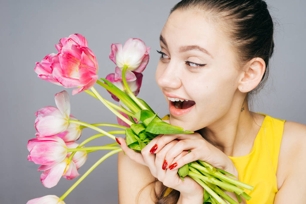 happy young girl in yellow dress holds pink fragrant flowers in hands, laughs and enjoys spring - Photo, Image