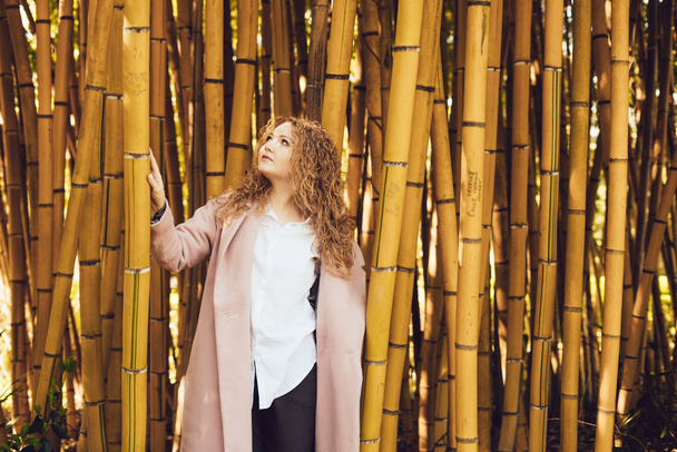 curly elegant woman posing next to bamboo deerviami in park, resting - Foto, afbeelding