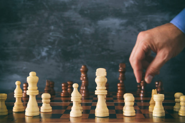 Εικόνα του επιχειρηματία χέρι κινείται σκάκι σχήμα πάνω από την σκακιέρα. Έννοιας επιχείρηση, ανταγωνισμός, στρατηγική, ηγεσία και επιτυχία. - Φωτογραφία, εικόνα