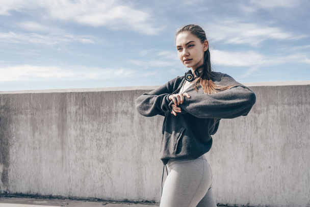 slender young girl in stylish sports clothes kneads muscles before training in the open air - Valokuva, kuva