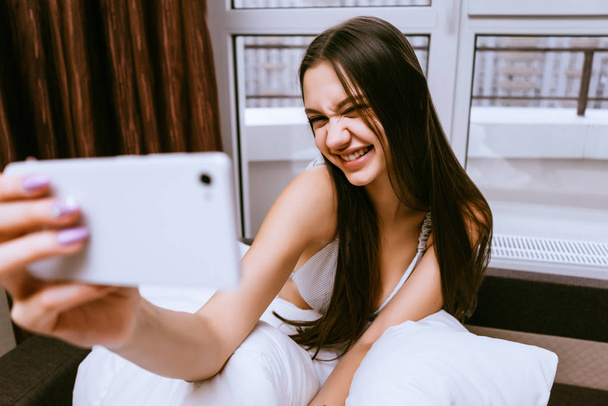 funny beautiful young girl sitting in bed early in the morning and doing selfie, smiling - Φωτογραφία, εικόνα