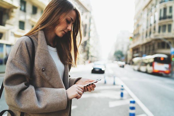 Piękna młoda kobieta nosi stylowe ubrania za pomocą smartfona podczas spaceru na ulicy - Zdjęcie, obraz