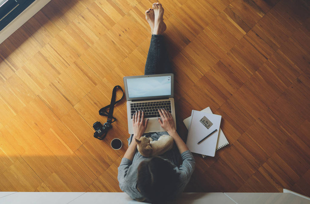 top view of a young female photographer works with a laptop while sitting on the wooden floor  - Φωτογραφία, εικόνα