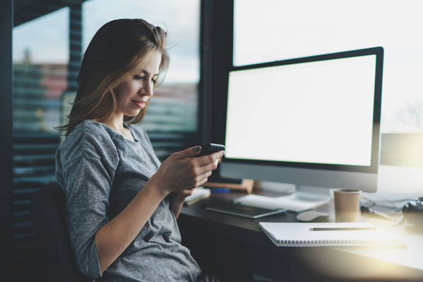 young female freelancer writing a text message on a modern mobile phone while sitting in the workplace in the home office  - Foto, Imagem
