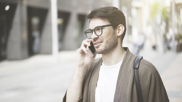 A closeup of smiling young man having a call on the street - Photo, Image