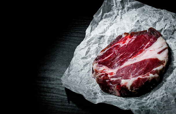 piece of raw meat beef steak on paper on dark wooden background with copy space. - Foto, Imagem