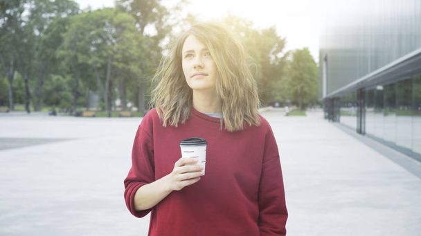 A young cute casual brunette girl is drinking coffee outside in the morning - Fotó, kép