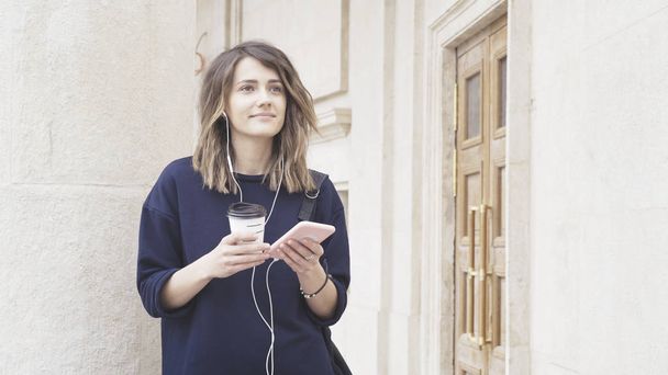 A smiling brunette white girl is listening to music outdoors - Φωτογραφία, εικόνα