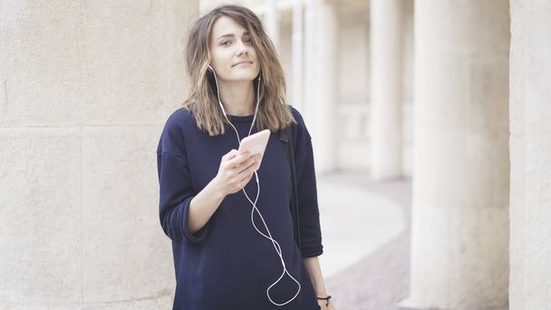 A smiling brunette white girl is listening to music outdoors - Photo, image