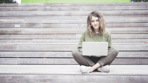 A young girl is working in a park with a laptop sitting on the stairs - Foto, Bild