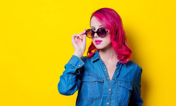 Young pink hair girl in sunglasses and blue shirt. Portrait on yellow background - Foto, Imagem