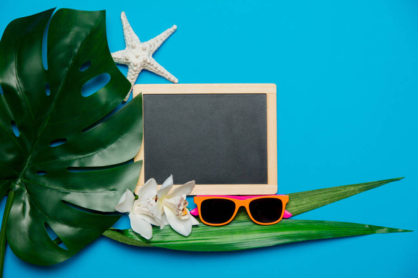 Tafel und Palmblatt mit Sonnenbrille. Objekte isoliert auf blauem Hintergrund - Foto, Bild