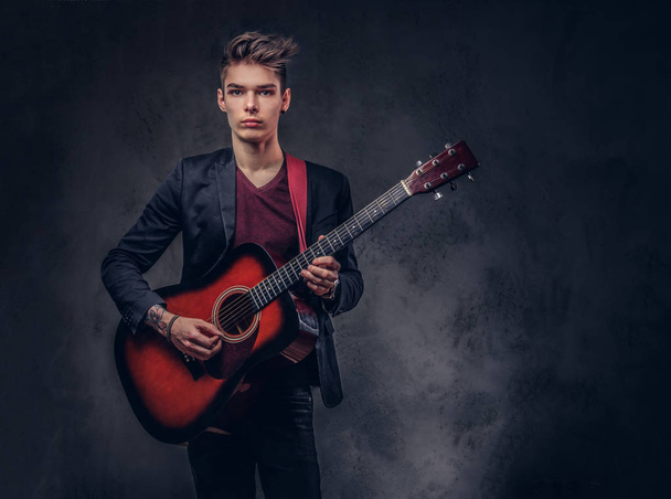Elegante joven músico con el pelo elegante en ropa elegante, tocando en una guitarra acústica
. - Foto, Imagen