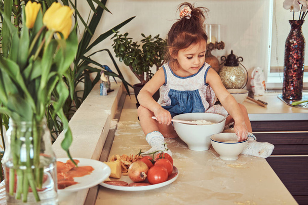 Sweet little cute girl learns to cook a meal in the kitchen. - Фото, изображение