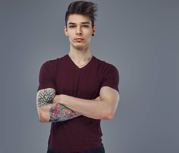 Guapo joven de moda con el pelo elegante y tatuaje en su brazo posando en un estudio
. - Foto, Imagen