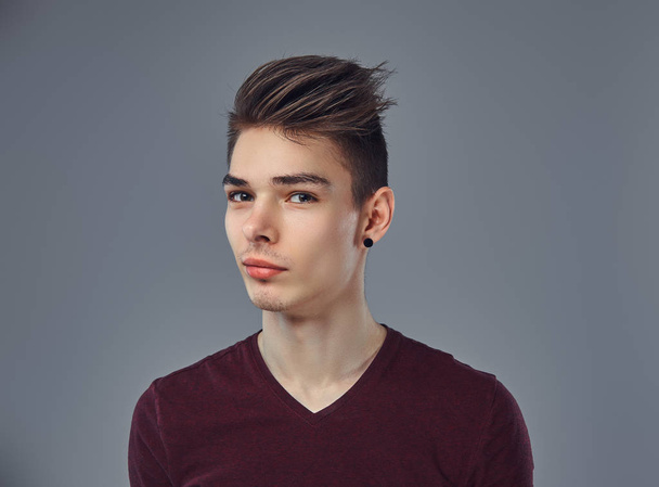 Guapo joven de moda con el pelo elegante y tatuaje en su brazo posando en un estudio
. - Foto, Imagen