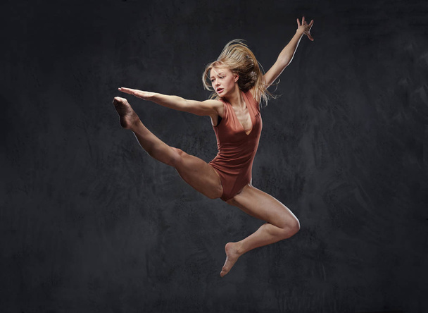 Young graceful ballerina dances and jumps in a studio. Isolated on a dark background. - Φωτογραφία, εικόνα