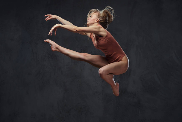 Young graceful ballerina dances and jumps in a studio. Isolated on a dark background. - Fotoğraf, Görsel