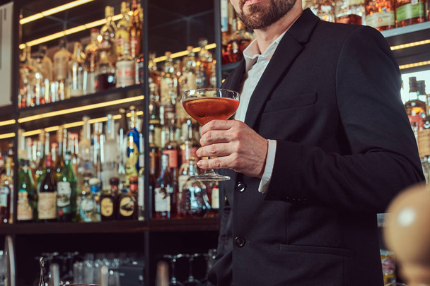 Szép, elegáns férfi tart egy pohár kizárólagos alkohol állandó, bár counter háttér. - Fotó, kép