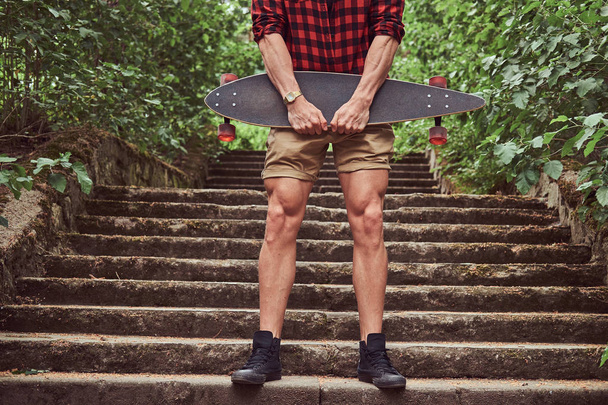 Cropped image of a muscular skater, standing on steps, holds the skateboard. - Photo, Image