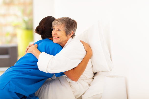 ευτυχής ηλικιωμένη γυναίκα που αγκαλιάζει φροντιστής στο κρεβάτι - Φωτογραφία, εικόνα