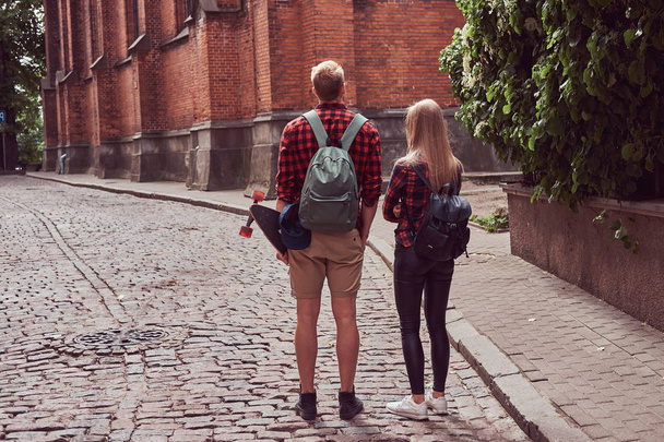 Giovane coppia hipster, bel pattinatore e la sua ragazza passeggiano per le vecchie strade d'Europa
. - Foto, immagini