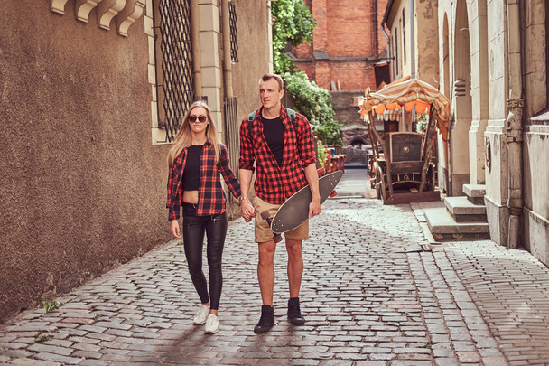 Jonge hipster paar, knappe schaatser en zijn vriendin lopen rond een oude smalle straatjes van Europa. - Foto, afbeelding
