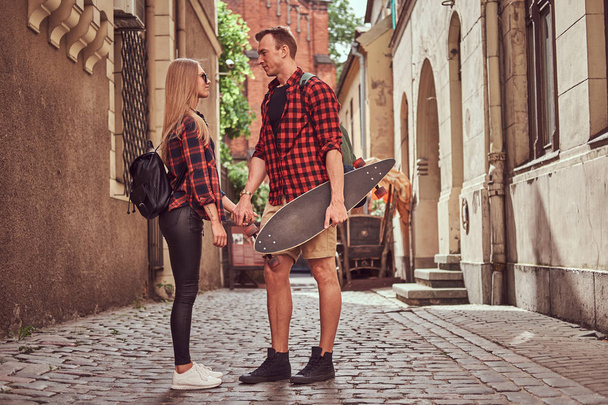 Para młoda hipster, przystojny łyżwiarz i jego dziewczyna stojąc na starych uliczek Europy. - Zdjęcie, obraz