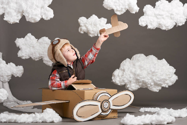 le garçon joue dans un avion en carton et rêve de devenir pilote, nuages de laine de coton sur fond gris
 - Photo, image