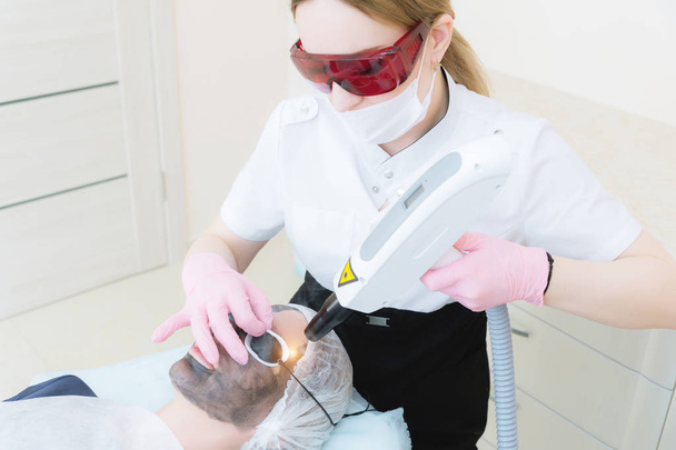 The cosmetician girl in goggles makes the procedure of carbon peeling with the help of a cosmetology laser. Carbon face peeling procedure. Laser pulses clean skin of the face. Hardware cosmetology - Foto, immagini