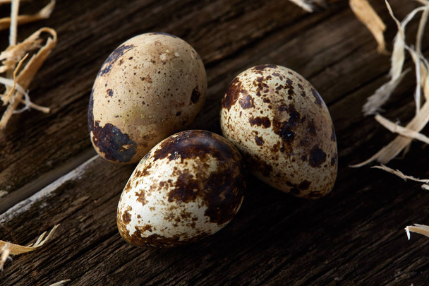 Conceptual still-life with quail eggs in hay nest over dark wooden background, close up, selective focus - Foto, Imagem