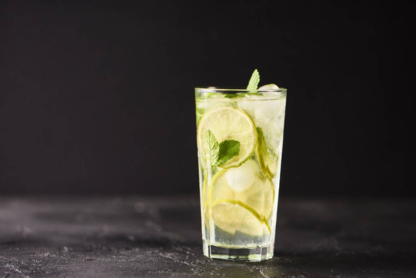 Mojito cocktail with limes and mint in highball glass on dark stone background. - 写真・画像