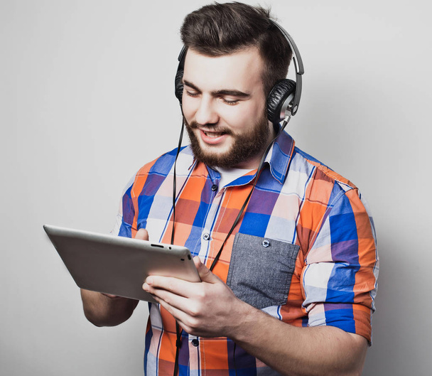 Studio portrait of a handsome bearded man using a tablet with headphones over a light grey  background. - Foto, immagini