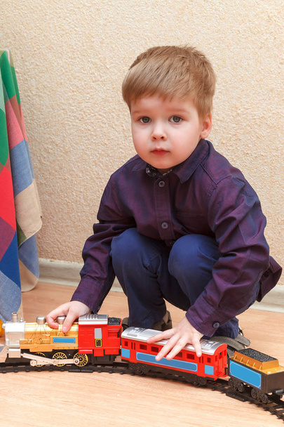 ein kleiner Junge spielt mit einer Eisenbahn, die auf dem Boden sitzt - Foto, Bild