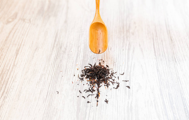 Samenstelling van natuurlijke zwarte thee met een blaadjes van de roos. Macro foto van thee bloemblaadjes op een houten lepel met een roos. Thee met de ingrediënten van bloemen en thee gelegen op een houten bord. - Foto, afbeelding