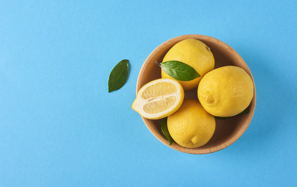 Fresh yellow lemons in wooden bowl on blue background with space for your text - Photo, Image