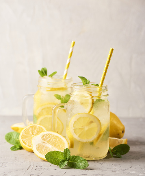 Verse lekkere limonade in mason glazen potten op witte concrete achtergrond - Foto, afbeelding