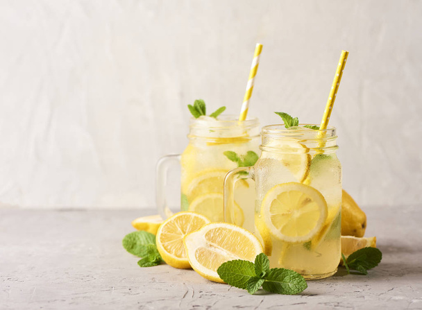 Fresh tasty lemonade in mason glass jars on white concrete background - Фото, изображение